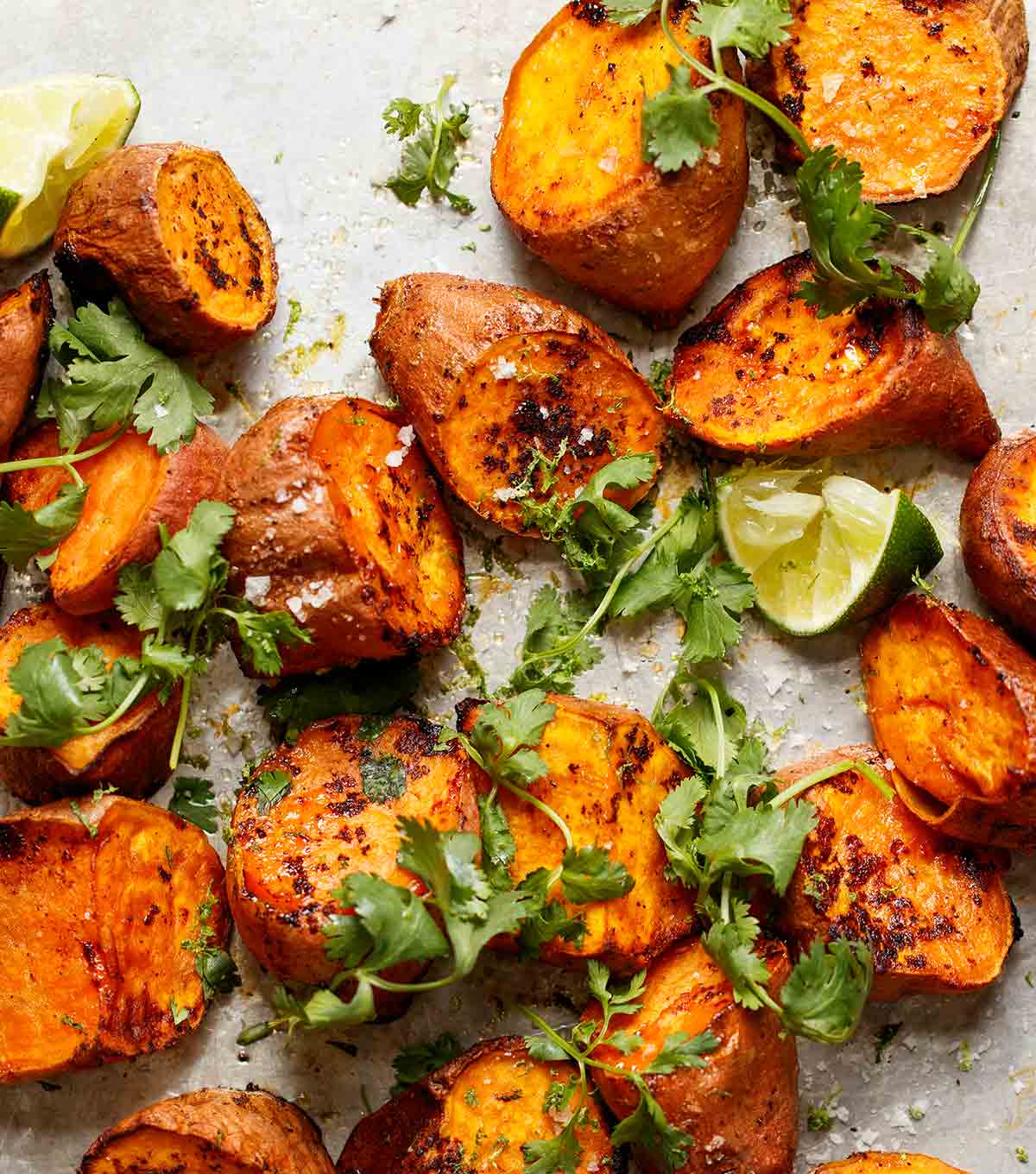 Chunks of roasted sweet potatoes with Sriracha and lime wedges and sprigs of cilantro scattered over the top.