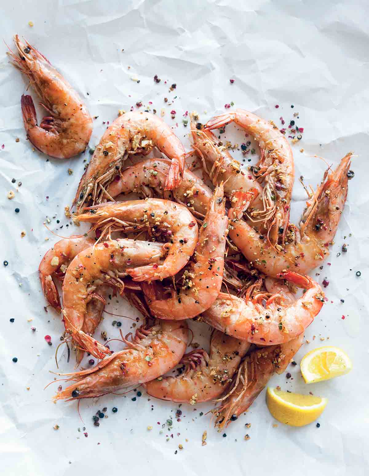 A pile of salt and pepper shrimp and lemon wedges on white paper