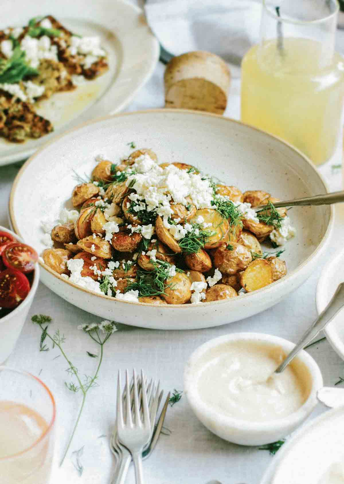White bowl filled with salt and vinegar roasted potatoes topped with crumbled feta cheese and oregano