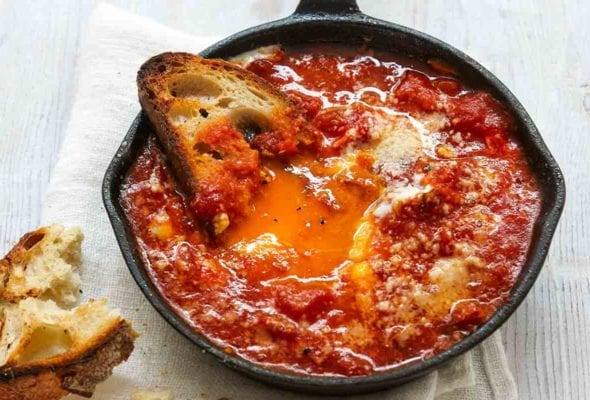 A small cast-iron skillet filled with eggs in hell, and half a piece of toasted bread.
