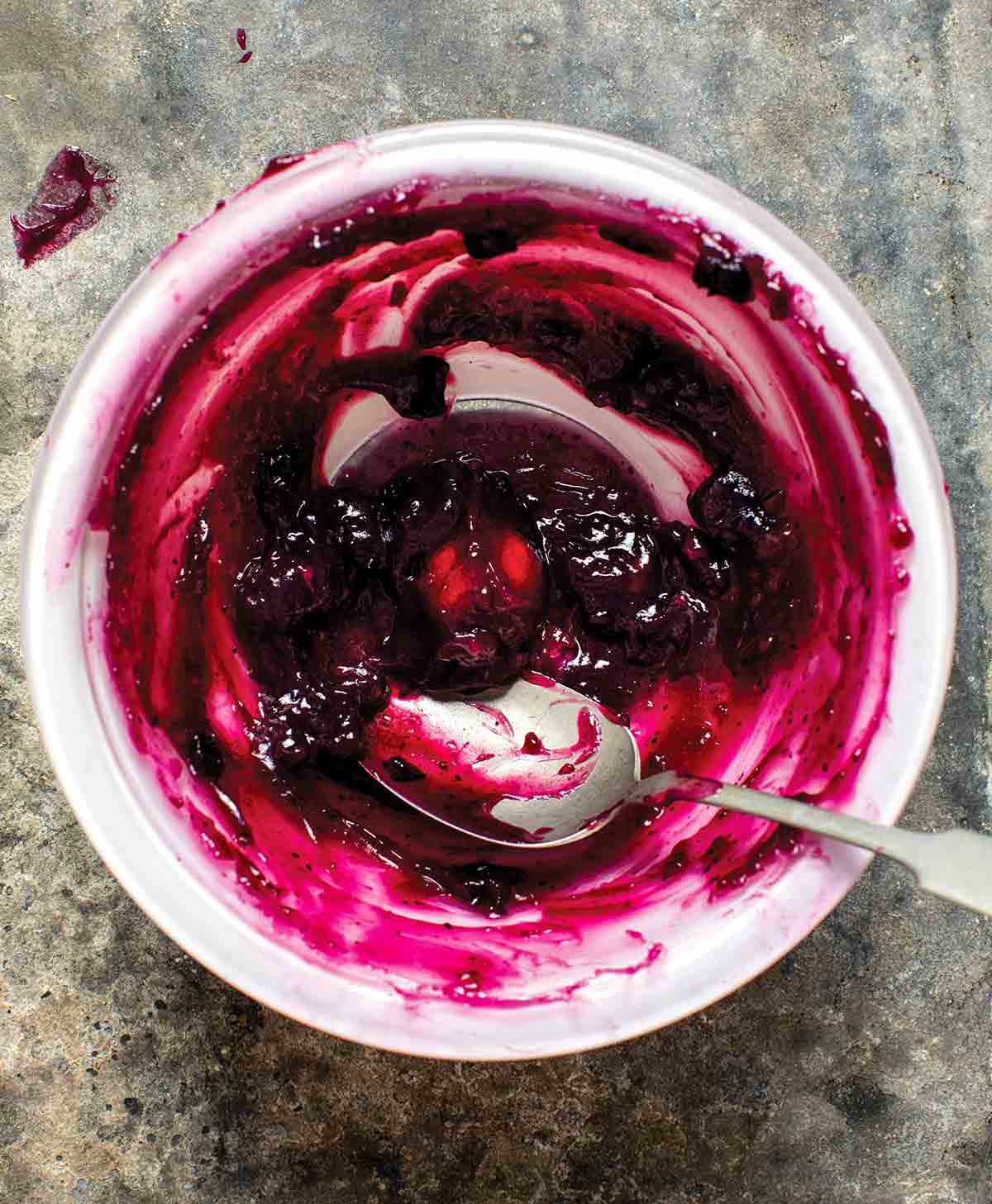 A white bowl with a little bit of stovetop fruit pie filling in the bottom and a spoon resting inside.