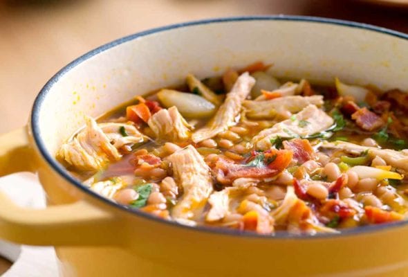 A yellow Dutch oven filled with white bean and chicken chili, topped with pieces of bacon.