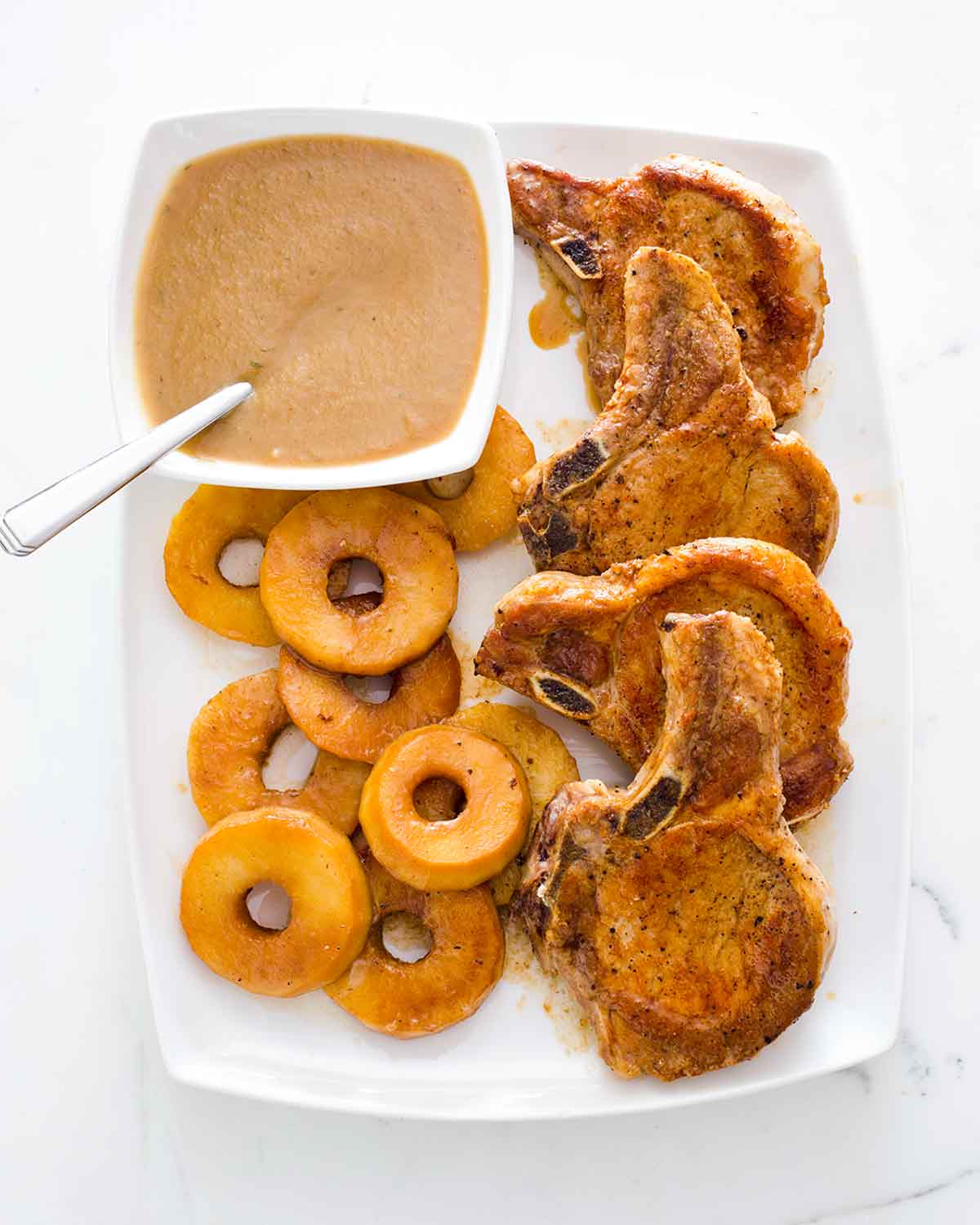 Four French-style pork chops with apples and Calvados sauce on a white platter.