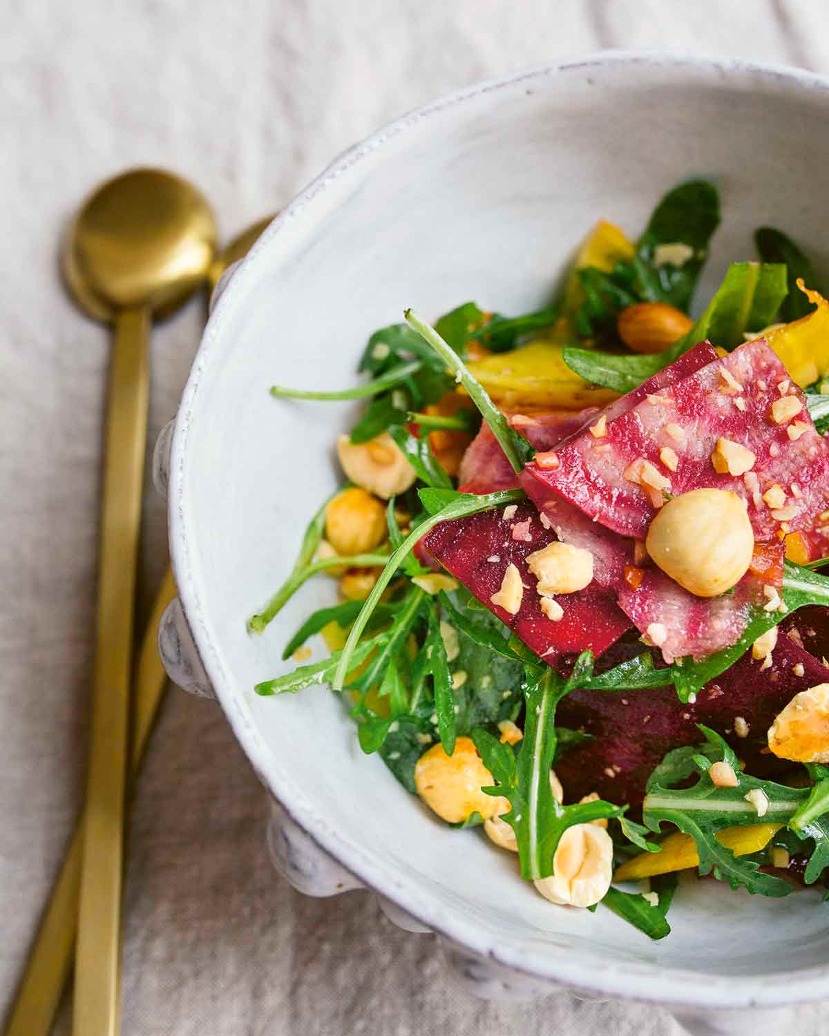 A white bowl filled with raw beet and hazelnut salad with a gold spoon beside the bowl.