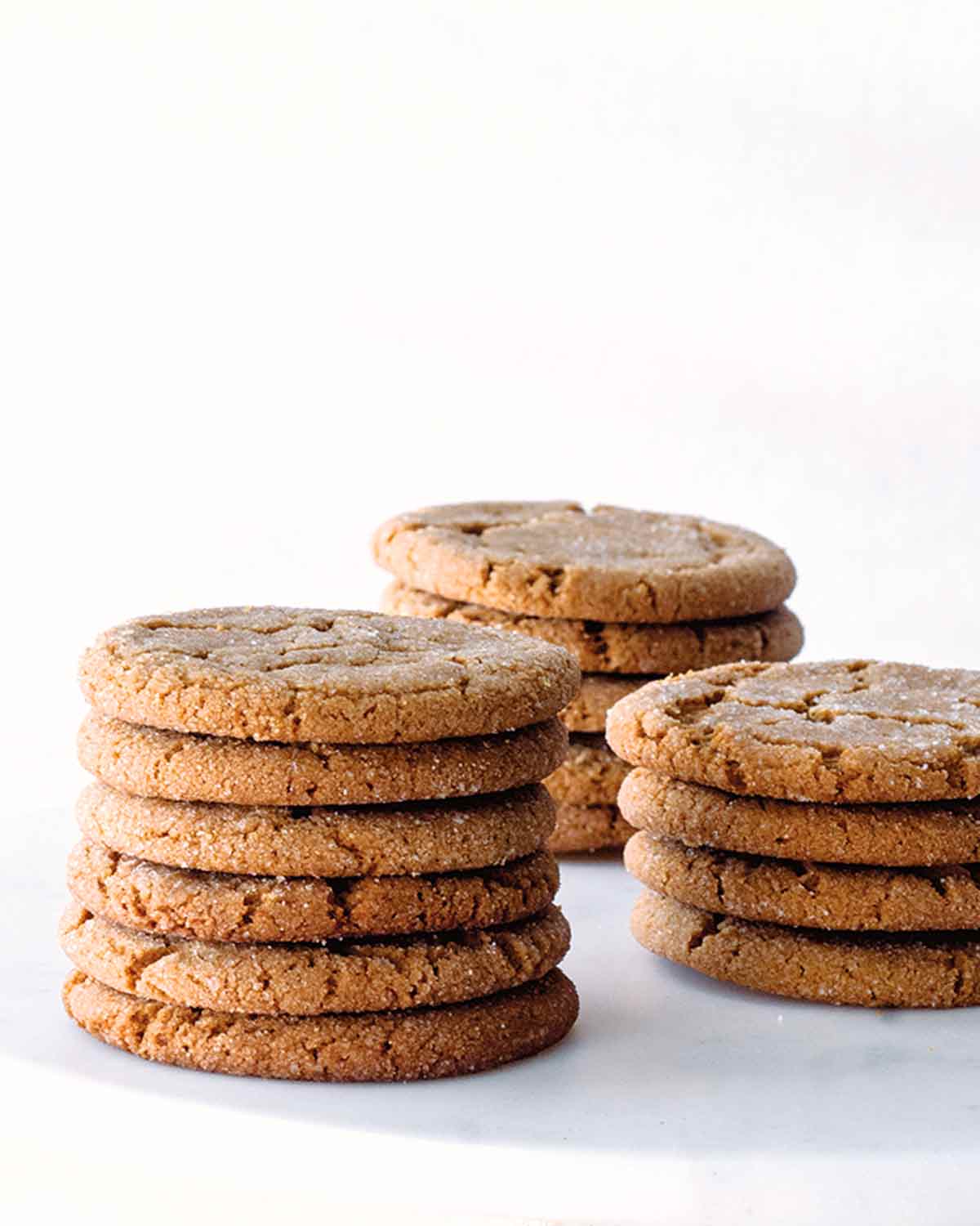 Three stacks of chewy molasses cookies on a white marble cake stand.