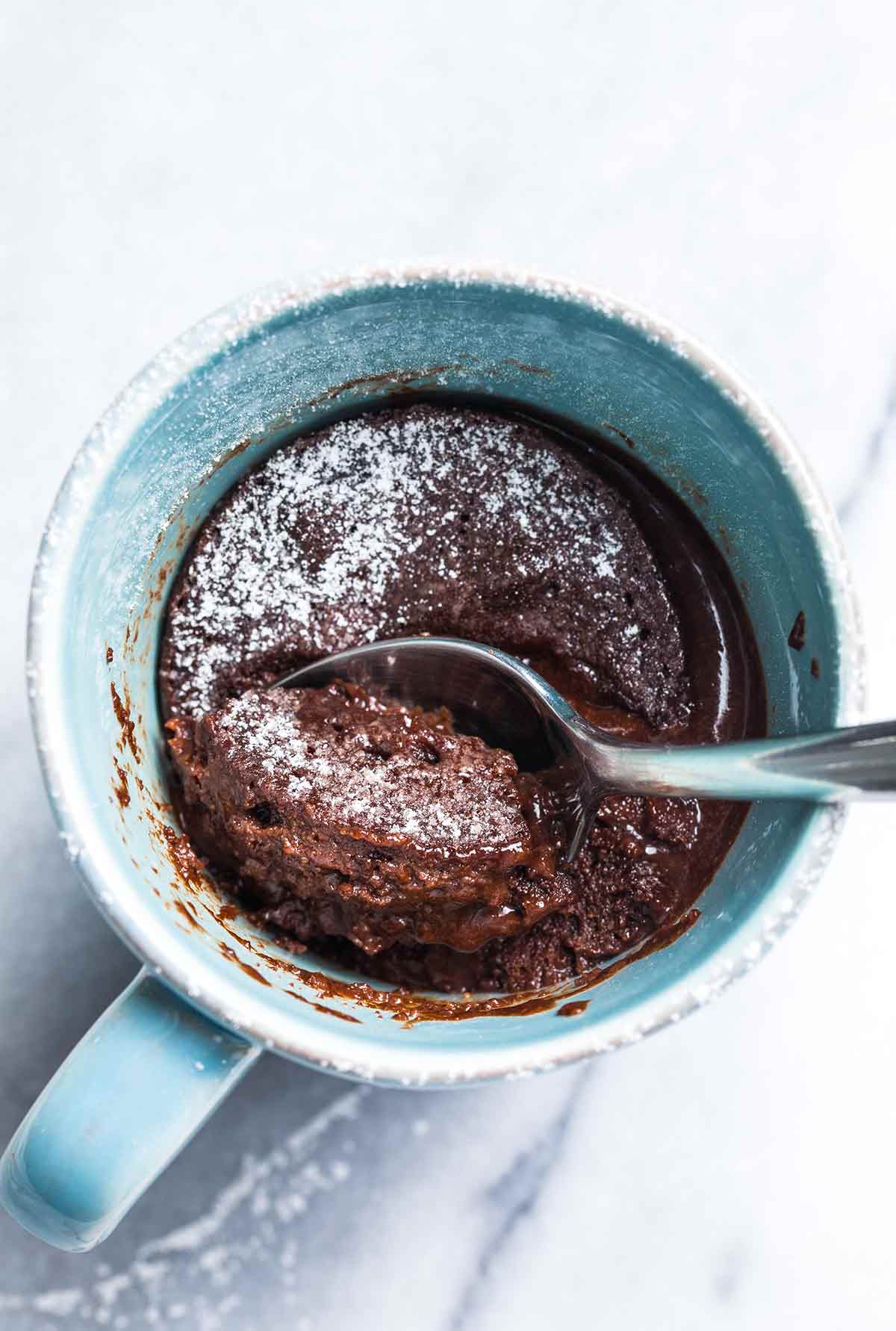 A spoon scooping chocolate mug cake from a blue mug.