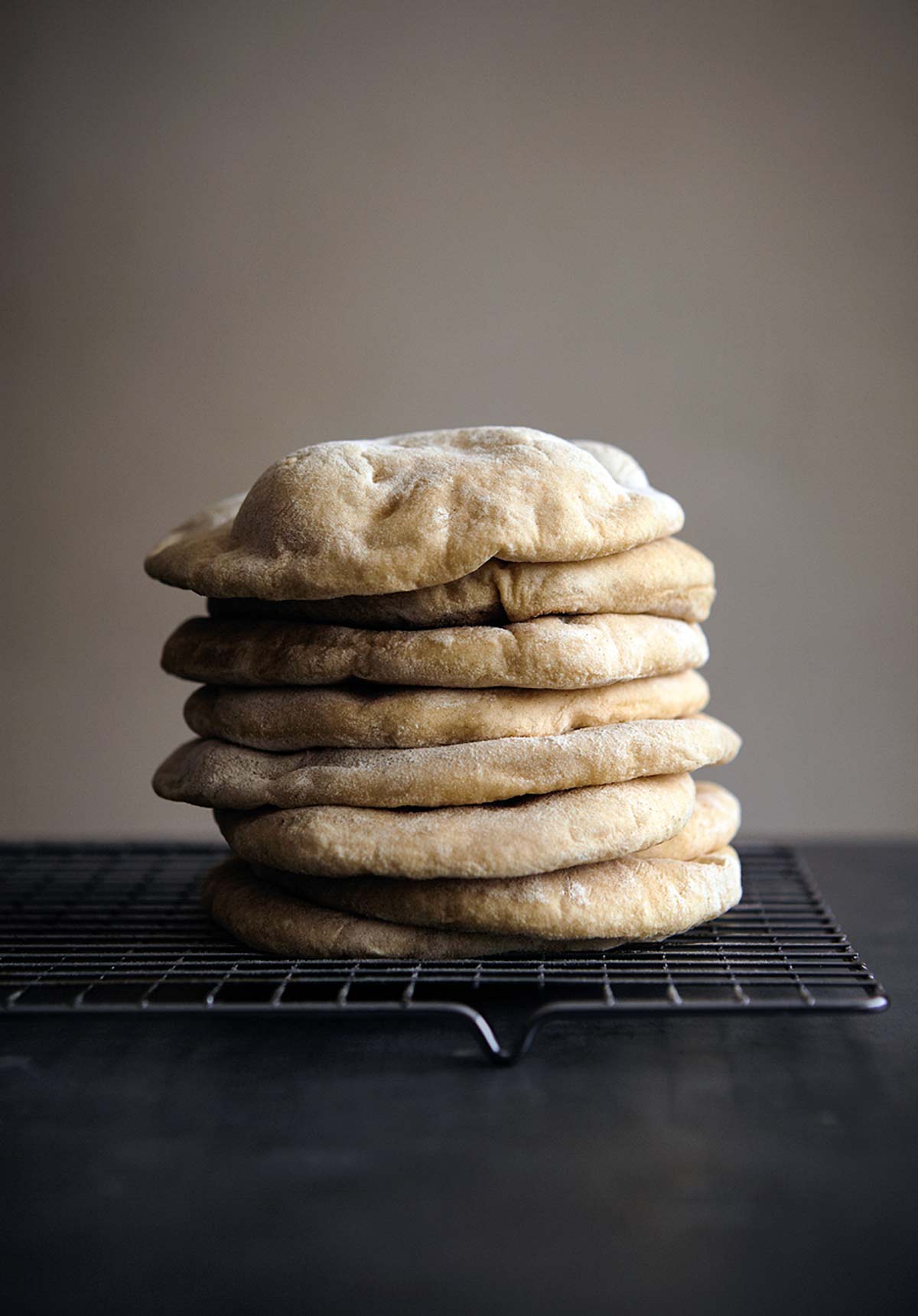 Nine homemade pita bread rounds stacked on a wire rack.
