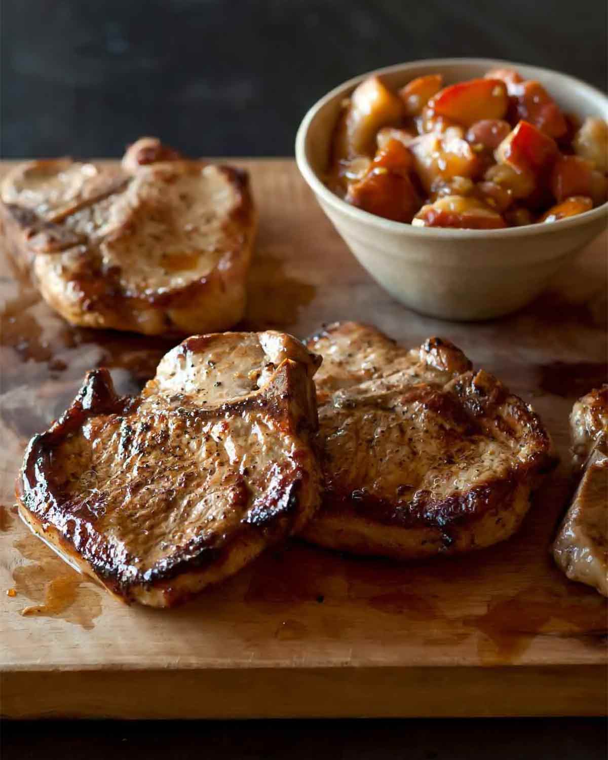 Four juicy seared maple-brined pork chops with pear chutney on a cutting board