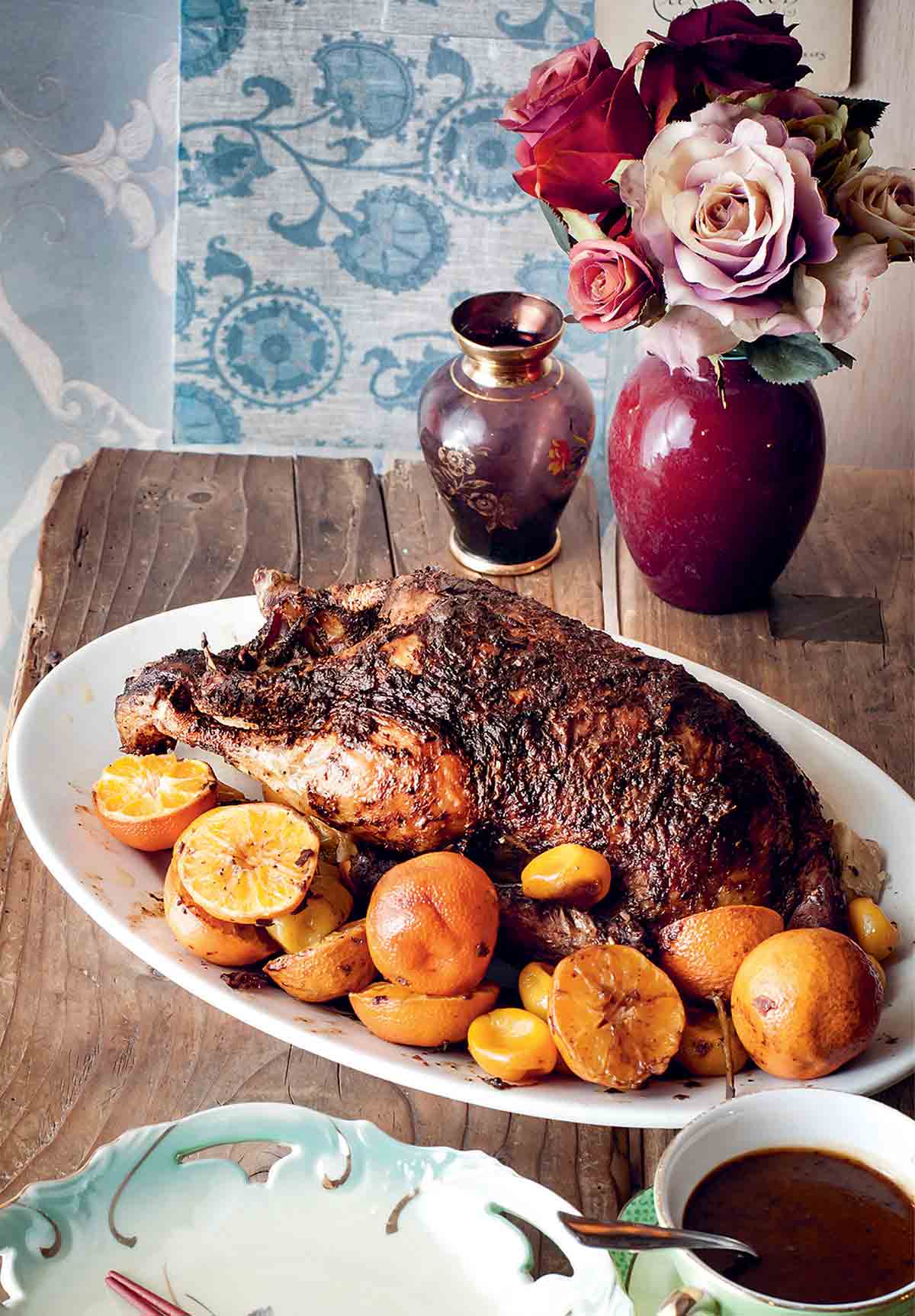 A white oval platter holding a whole roast duck with clementines scattered around it.