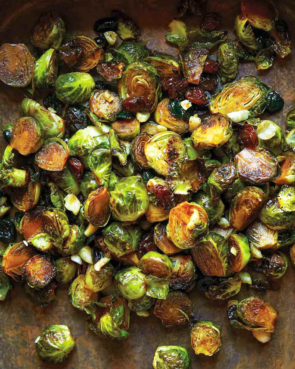 Spicy roasted Brussels sprouts with dried cranberries and macadamia nuts on a baking sheet.