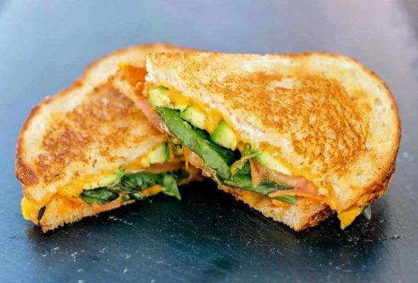 A veggie grilled cheese sandwich sliced in half on a glass platter