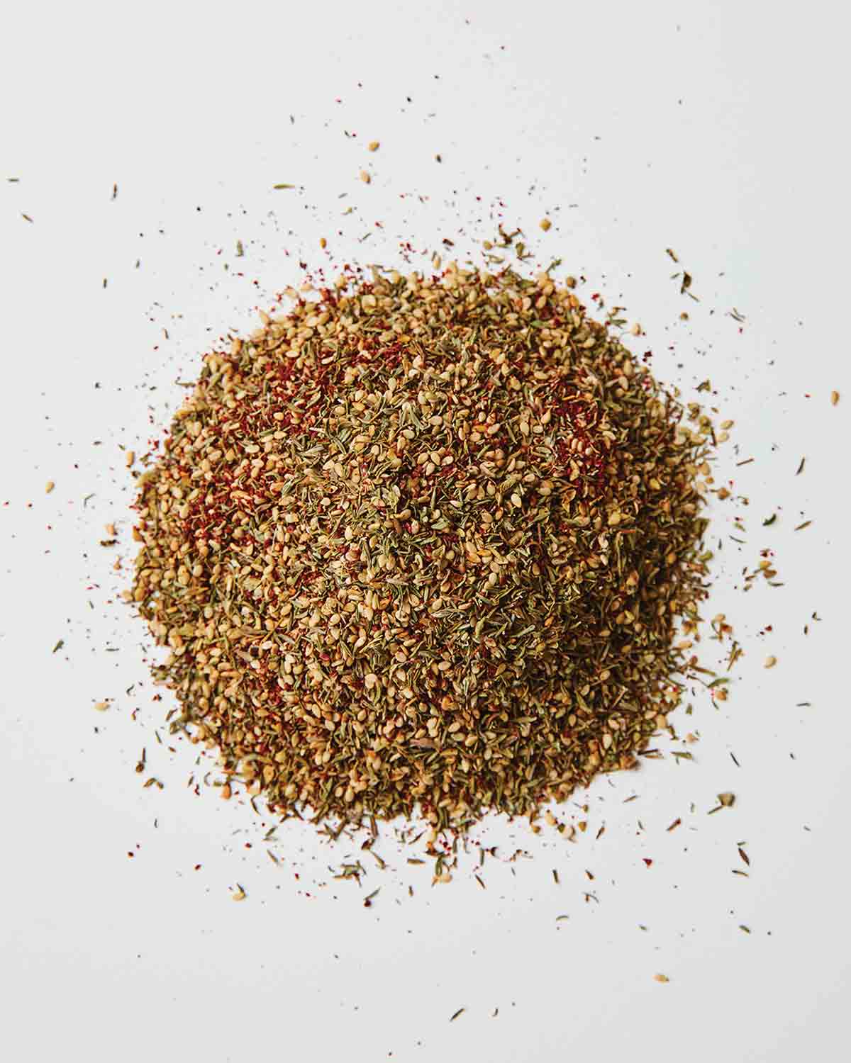 A scoop of za'atar spice blend on a white background.