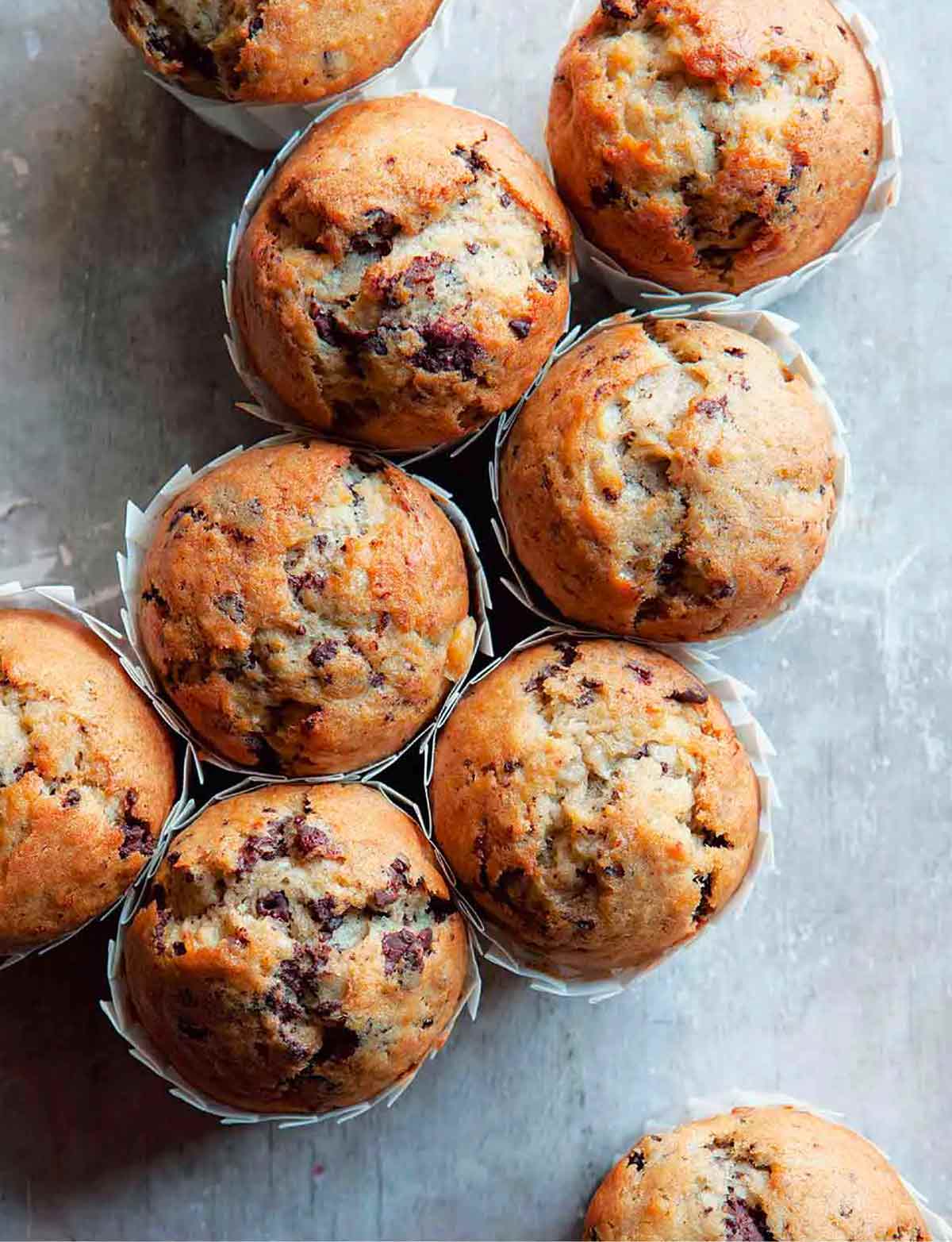 Nine banana muffins with white wrappers.