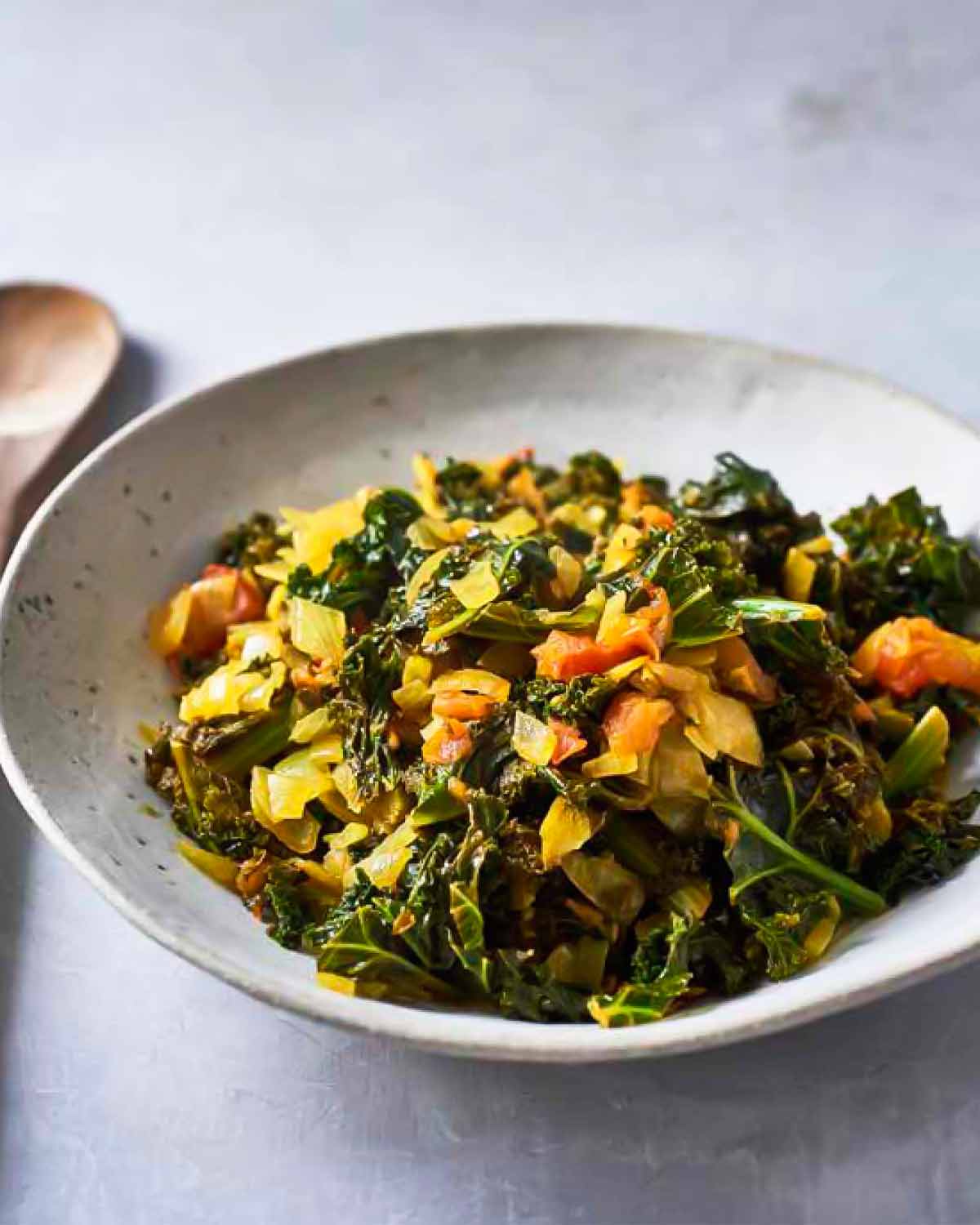 A ceramic bowl filled with greens with tomatoes, or sukuma wiki.
