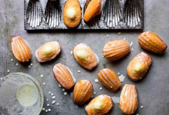 Several lemon madeleines next to a madeleine pan and a bowl of lemon glaze nearby.