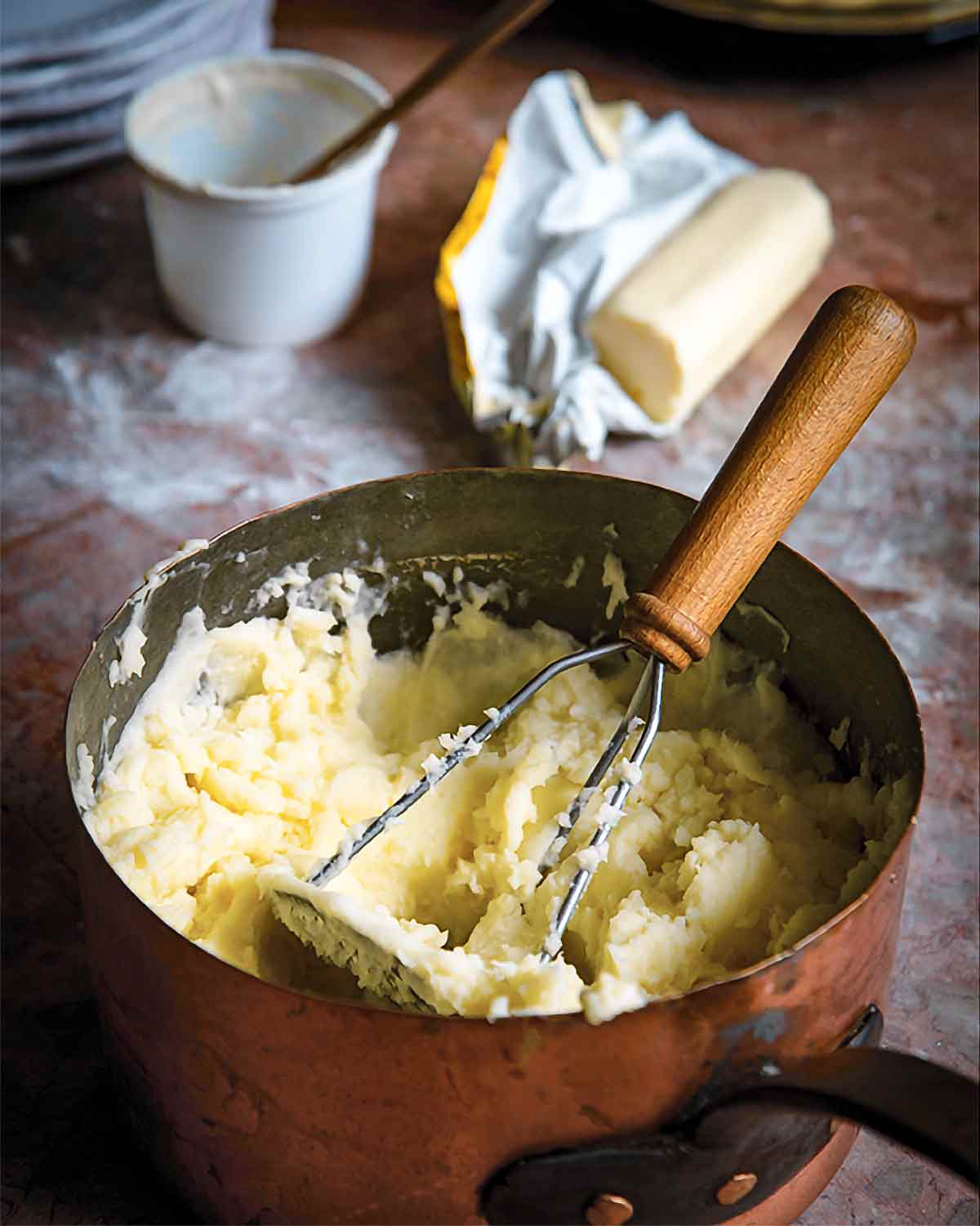 A copper pot filled with mashed potatoes with crème fraîche and a masher resting inside.