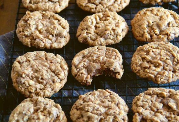 Several oatmeal chocolate chip cookies cooling on a rack, one with a bite out of it.