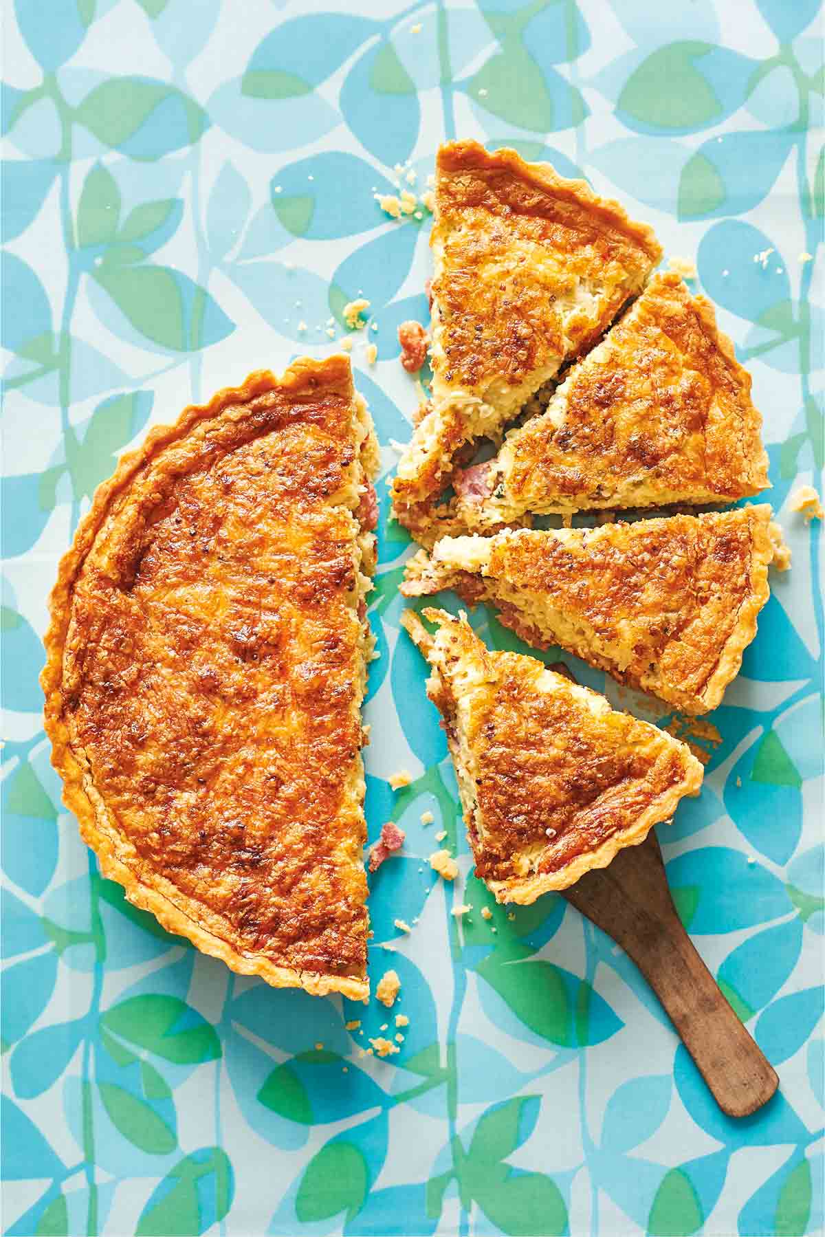 A quiche Lorraine cut in half, and half cut into quarters on a patterned background.