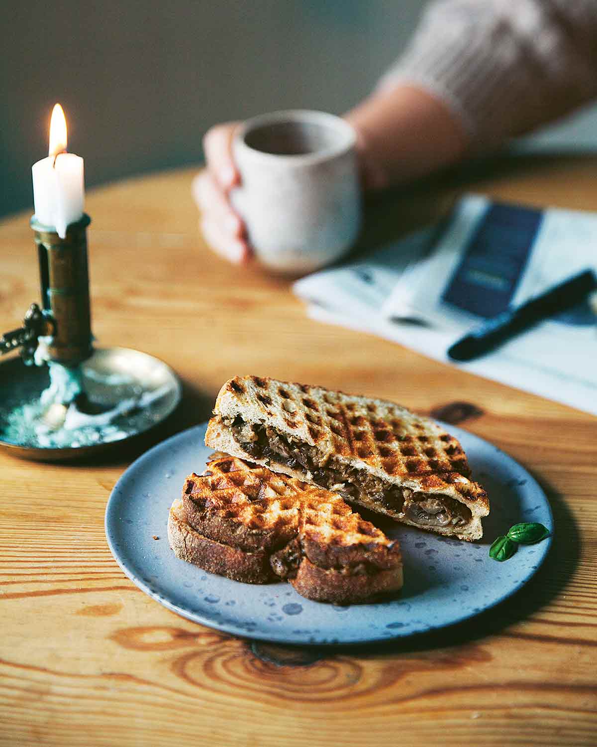 Two halves of waffle toasties with mushrooms on a blue plate with a candle beside it an a person in the background.