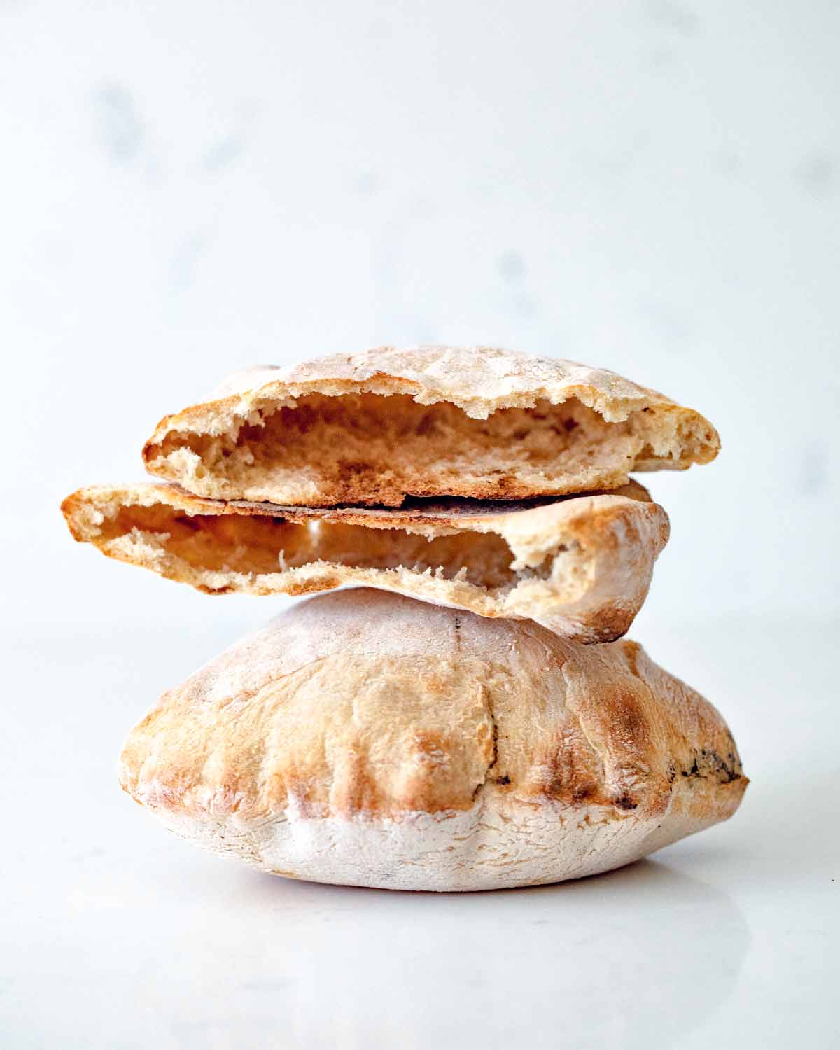 One whole and one torn whole grain sourdough pita stacked on top of each other.