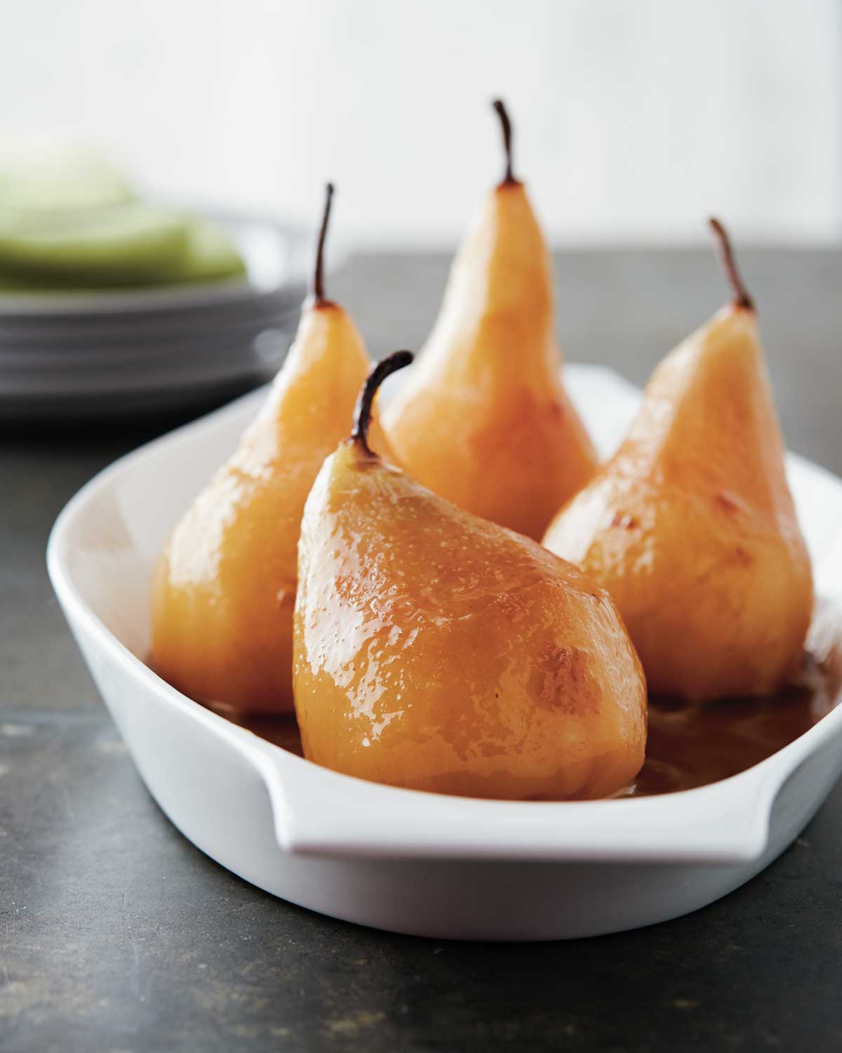 Four wine poached pears in a shallow white baking dish.