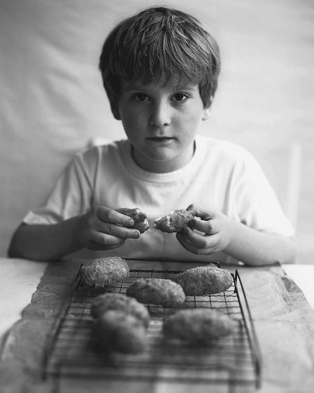 A boy opening an arancini with six more cooling on a rack in front of him.