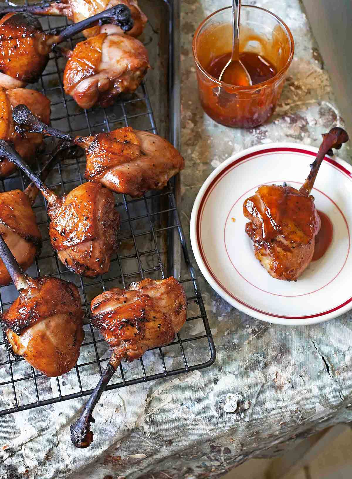Hoisin-glazed duck shanks on a wire rack and one on a plate with a jar of honey beside it.