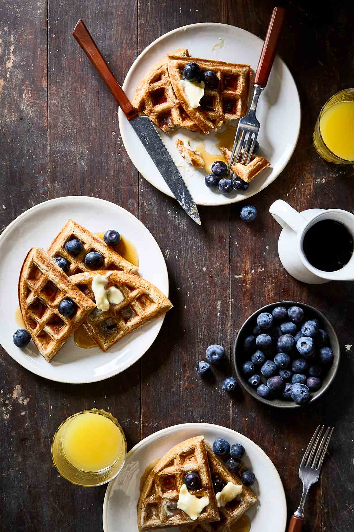 Two white plates with overnight sourdough waffles, blueberries, butter, and syrup on them.