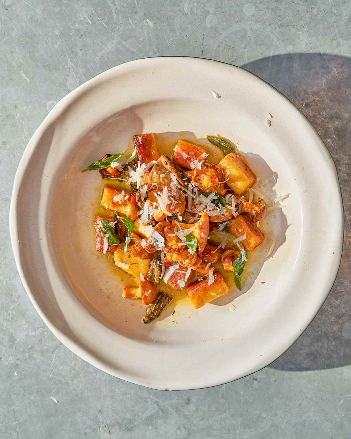 A white bowl filled with pan-roasted gnocchi sage, and mushrooms, with shredded Parmesan on top.
