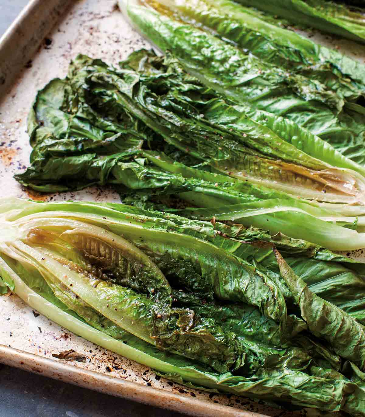 Halves of roasted romaine Caesar salad on a rimmed baking sheet.