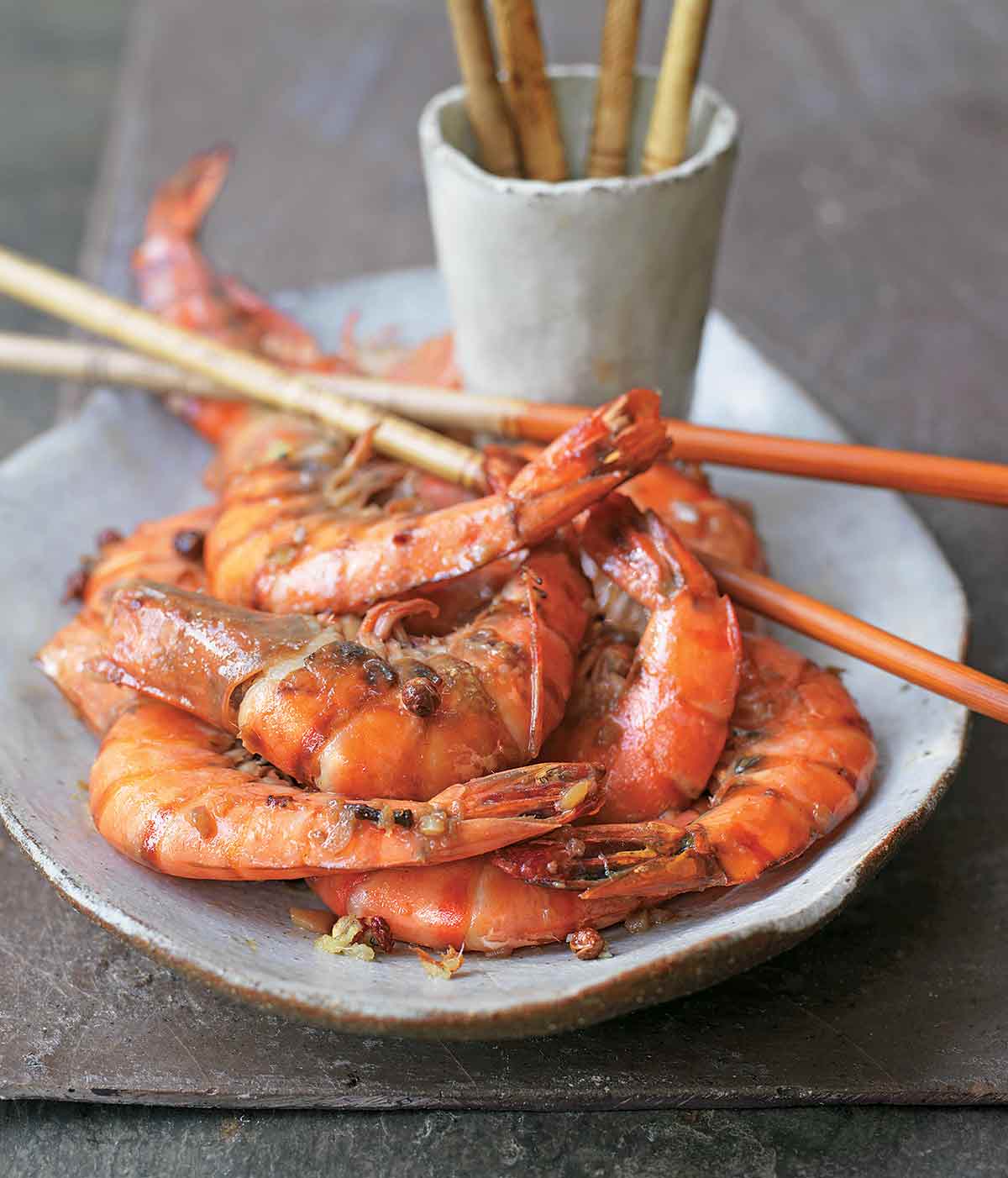 An oval ceramic platter topped with Sichuan pepper prawns and bamboo sticks crossed over the top of them.