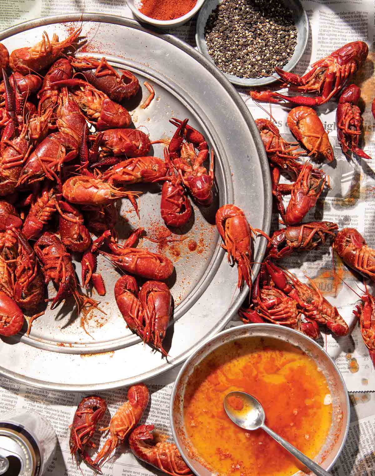 Crawfish piled on a platter and on newspaper beneath it with a bowl of butter beside for a tandoori masala crawfish boil.