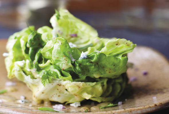 Leaves of butter lettuce with Maytag blue cheese on a brown speckled plate.