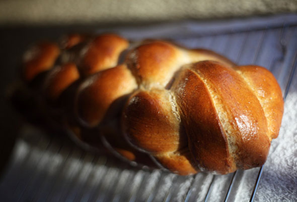 A loaf of braided challah on a wire rack.
