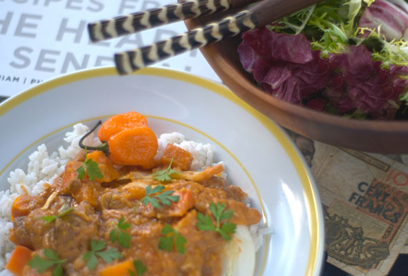 A yellow and white bowl filled with mafe, Senegalese lamb stew, with a habanero pepper on the side and a bowl of salad next to it.