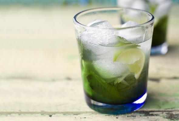 A short glass filled with a mint mojito, muddled mint leaves, a wedge of lime, and several ice cubes.